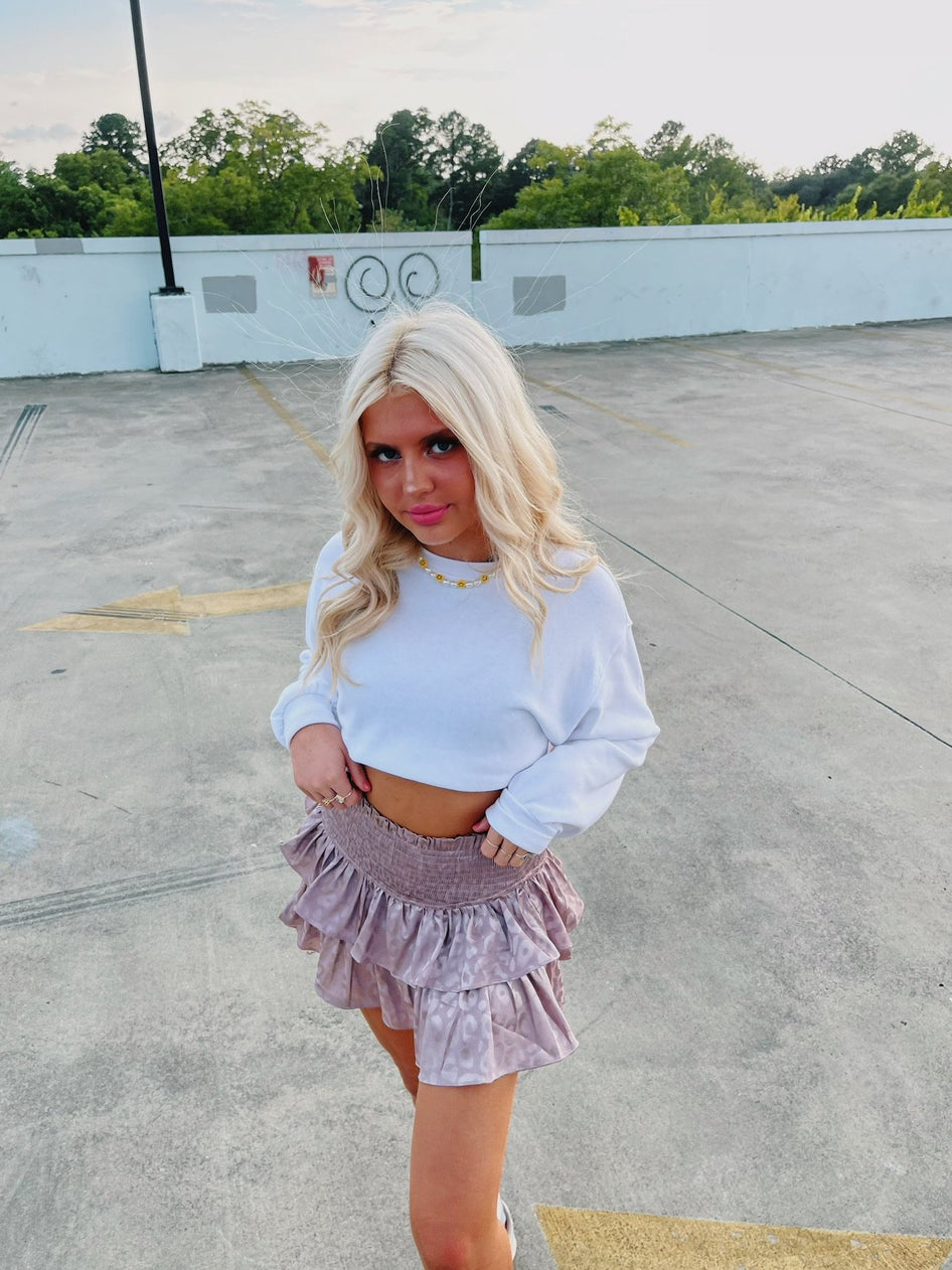Mauve ruffle mini skirt with subtle animal print, modeled outdoors.
