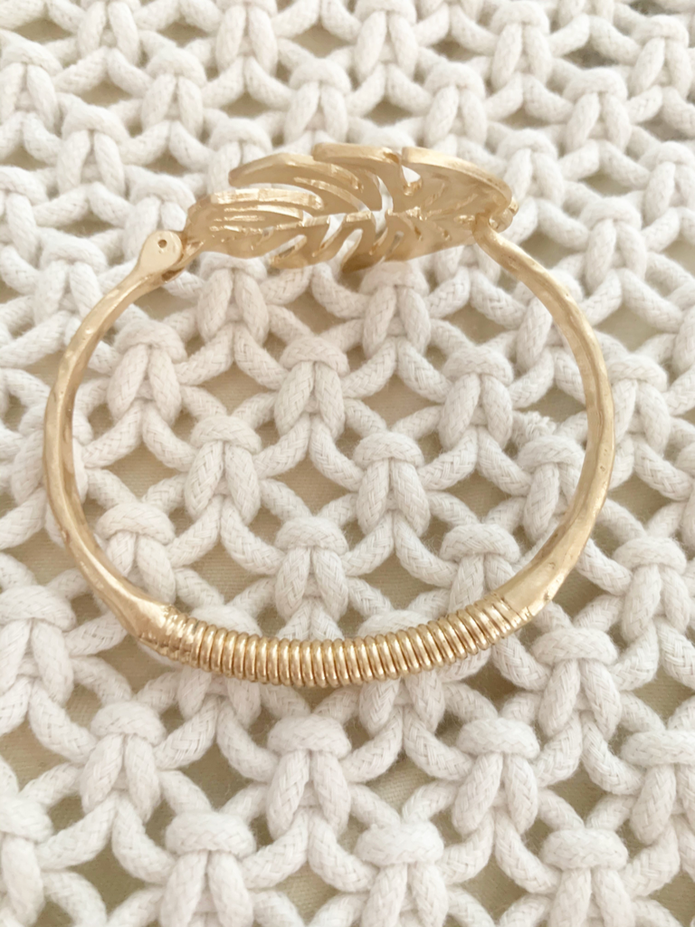 Gold leaf bangle bracelet on cream knit fabric.
