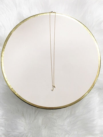 Gold music note charm necklace on blush pink display.
