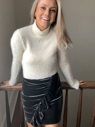 Charcoal gray velvet mini skirt with a ruffle detail, modeled indoors.
