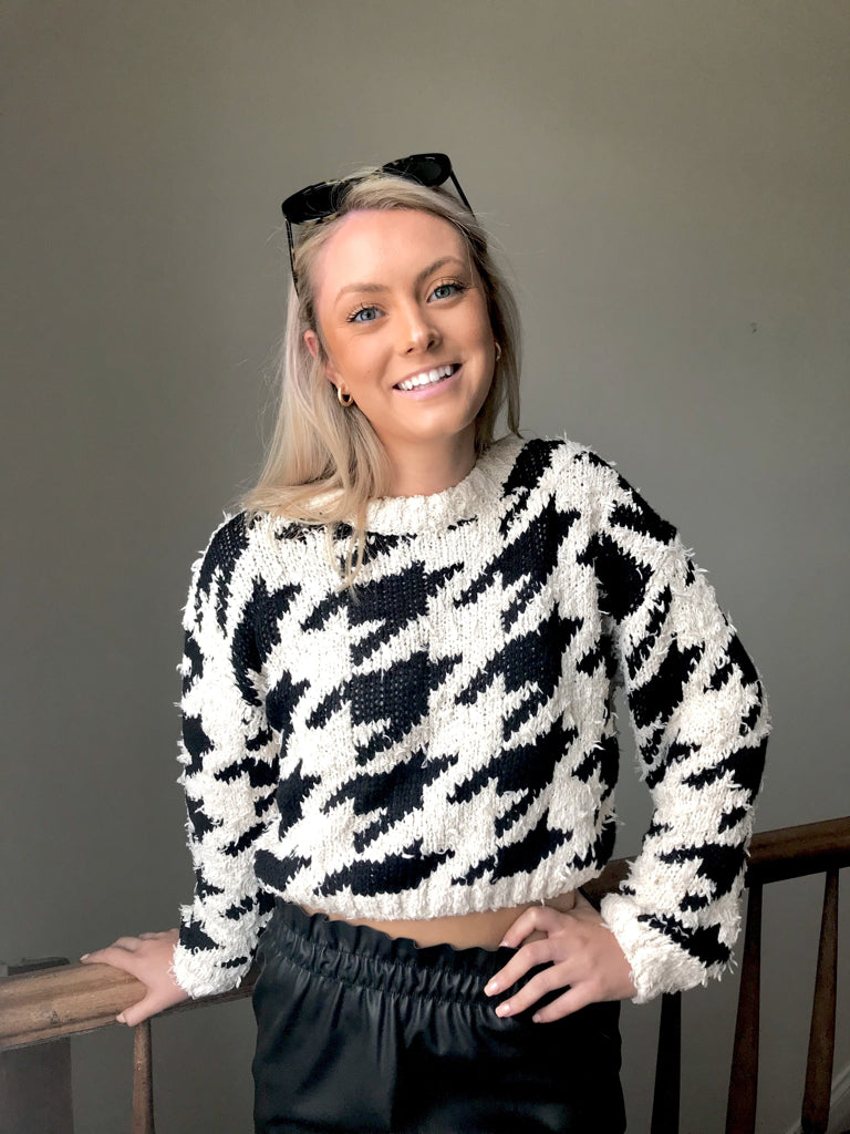Woman smiling, wearing a cropped black and white houndstooth knit sweater.
