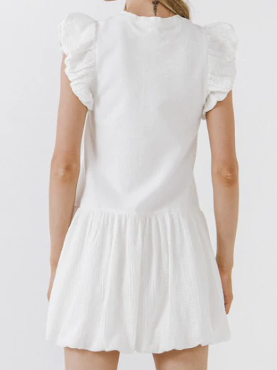 White eyelet mini dress with ruffled cap sleeves and a bubble hem, shown from the back.
