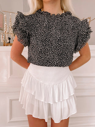 Black and cream leopard print blouse with ruffled sleeves, modeled with a white tiered skirt.
