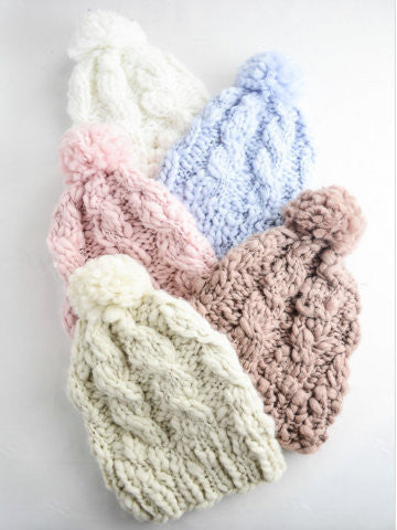 Cable knit beanie hats with pom-poms in pink, cream, light blue & mauve.
