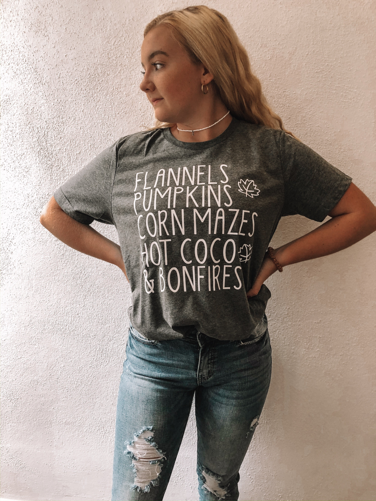 Gray fall-themed tee showcasing flannels, pumpkins, corn mazes, hot cocoa, and bonfires.
