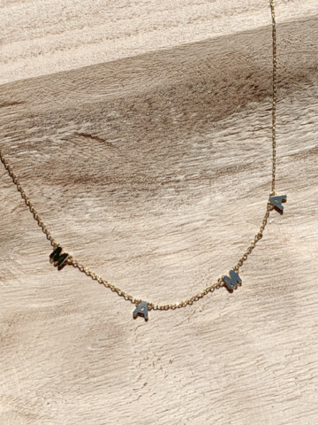 Gold chain necklace with "MAMA" letters, displayed on light wood background.
