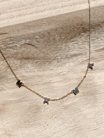 Gold chain necklace with "MAMA" letters, displayed on light wood background.
