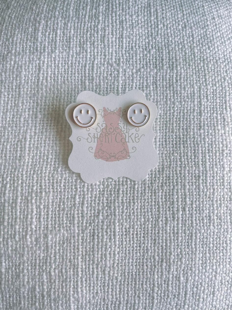 White smiley face stud earrings displayed on a textured white background.
