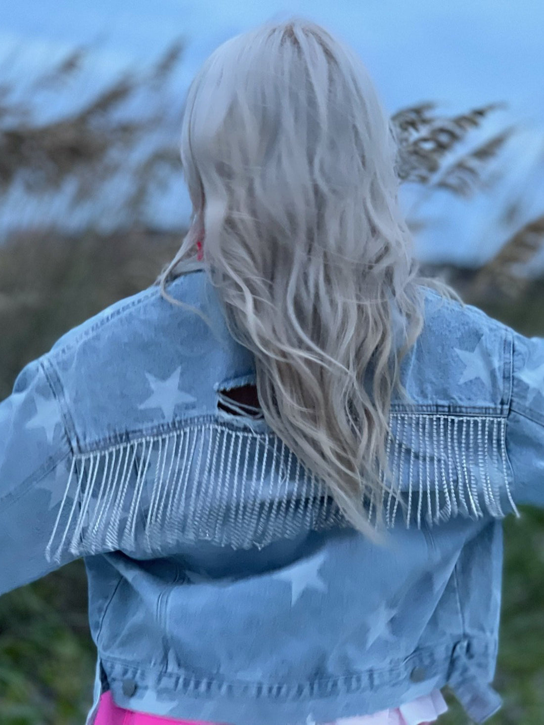Light wash denim jacket with star print and beaded fringe detail, worn outdoors.

