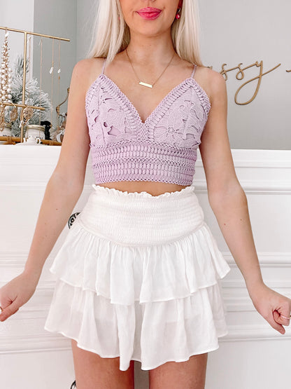 Lilac lace crop top paired with white tiered ruffle mini skirt, styled against a white wainscoted wall.
