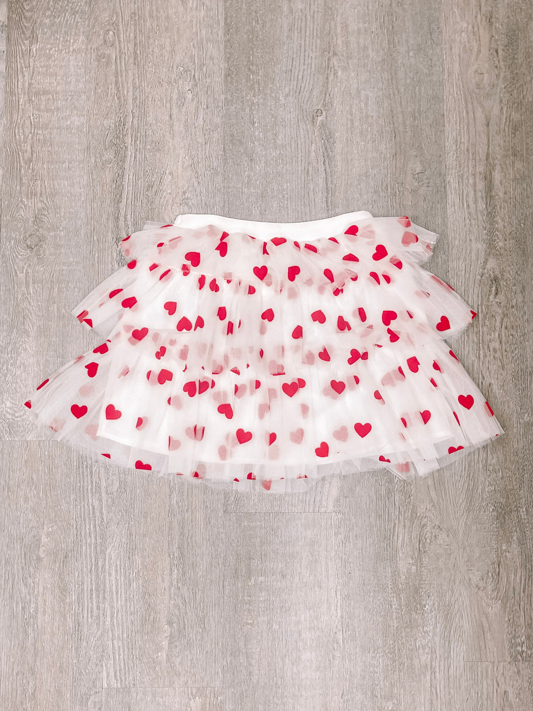 White tulle skirt with red hearts, layered design, flat lay on wood background.
