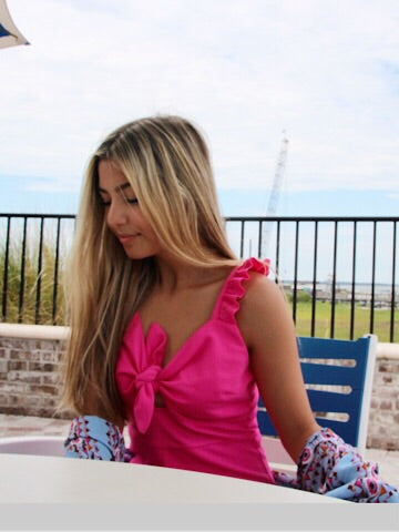 Hot pink romper with ruffle straps and a front tie detail, worn outdoors.
