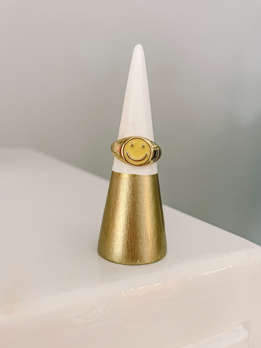 Gold smiley face ring displayed on a ring cone.
