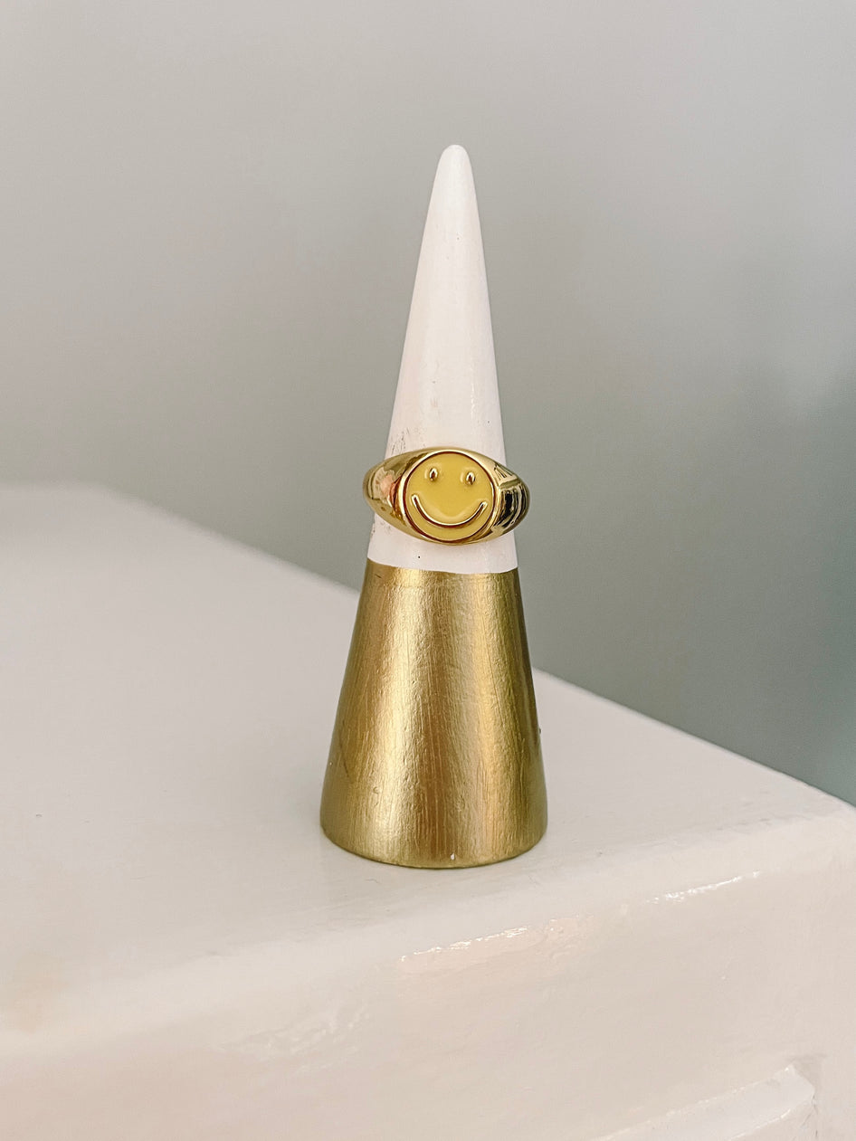 Gold smiley face ring displayed on a ring cone.
