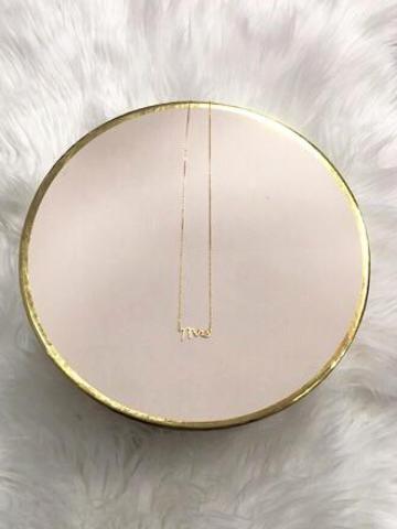 Gold "me" necklace on blush pink display
