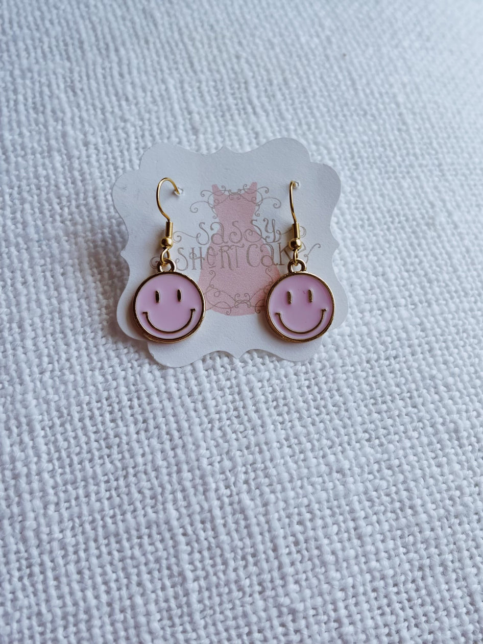 Pink smiley face earrings with gold hooks, cheerful and fun.
