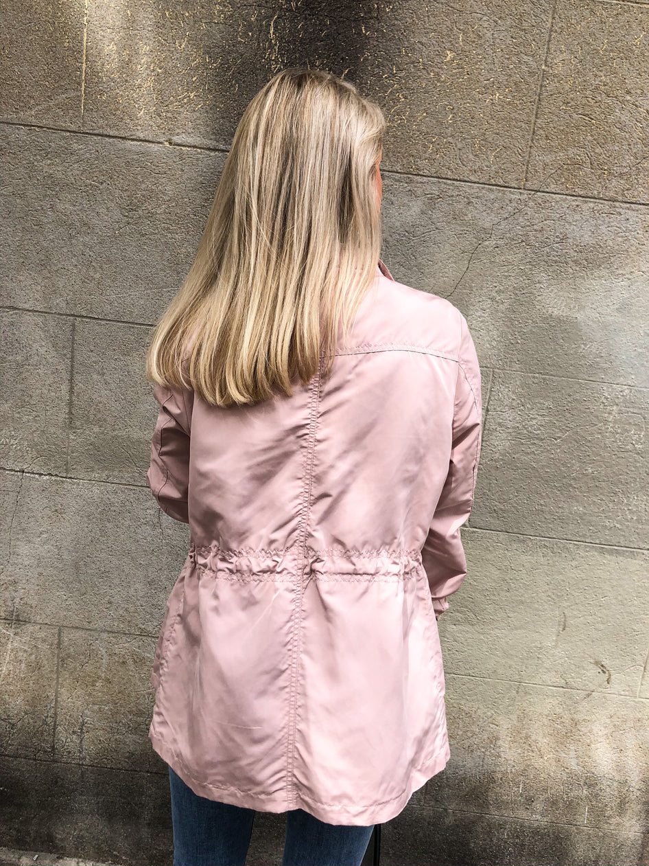 Dusty rose lightweight jacket, rear view, against a textured stone wall.
