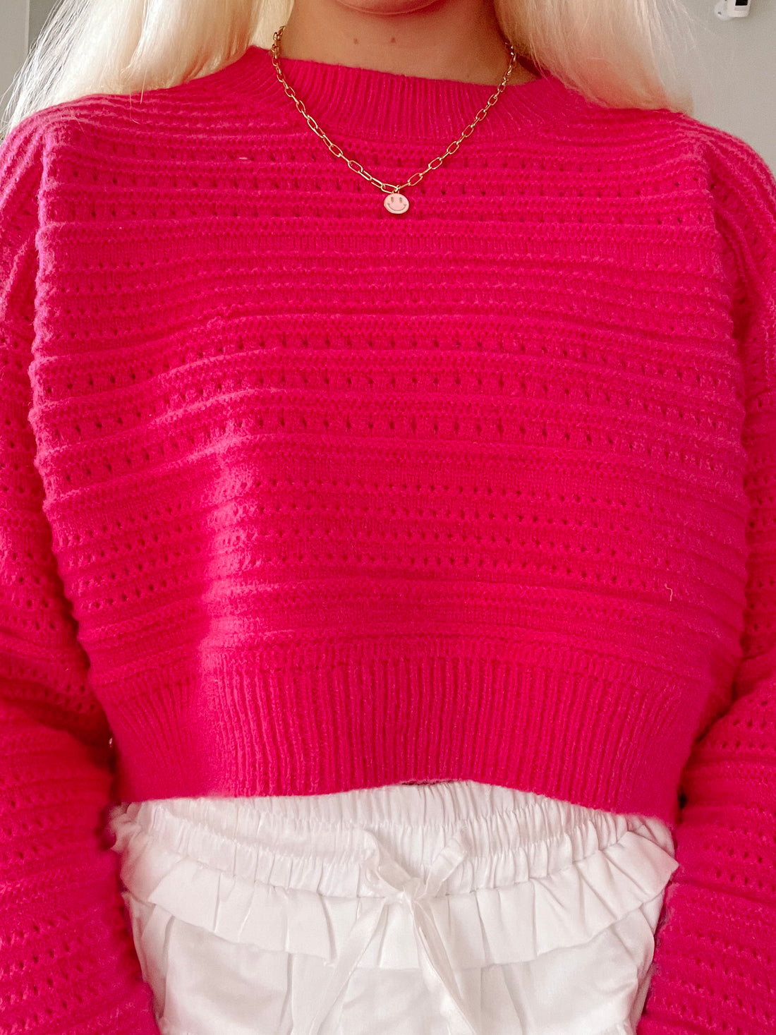Hot pink cropped knit sweater with eyelet detailing, shown paired with white shorts.
