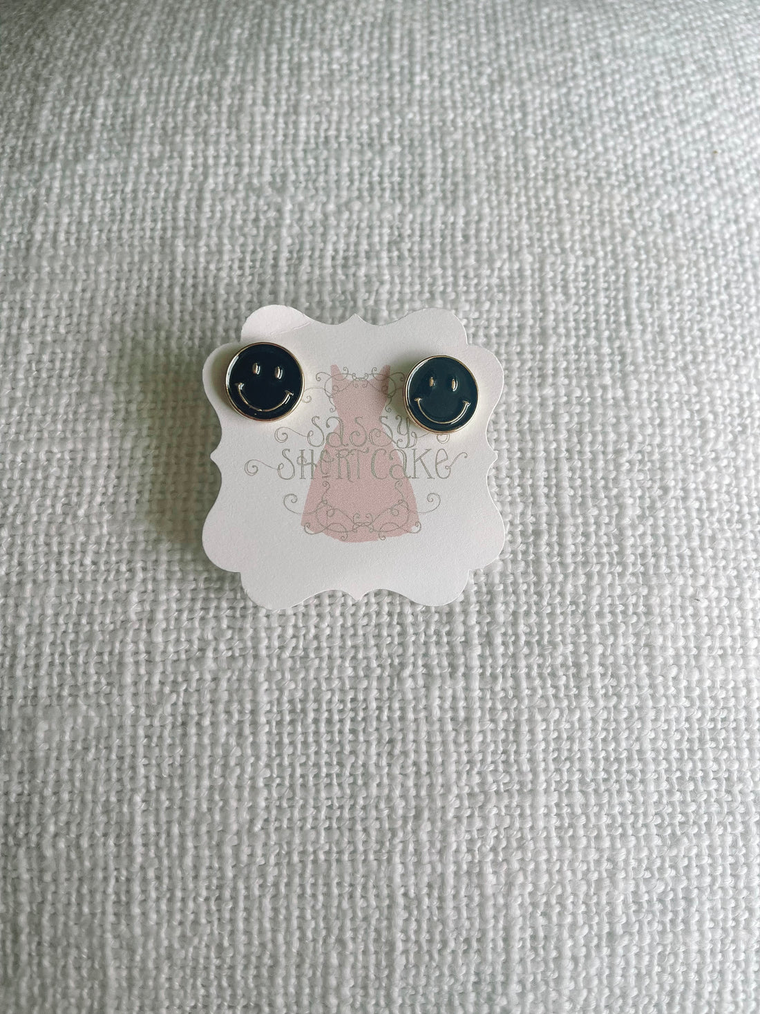 Black smiley face stud earrings displayed on a white textured background.
