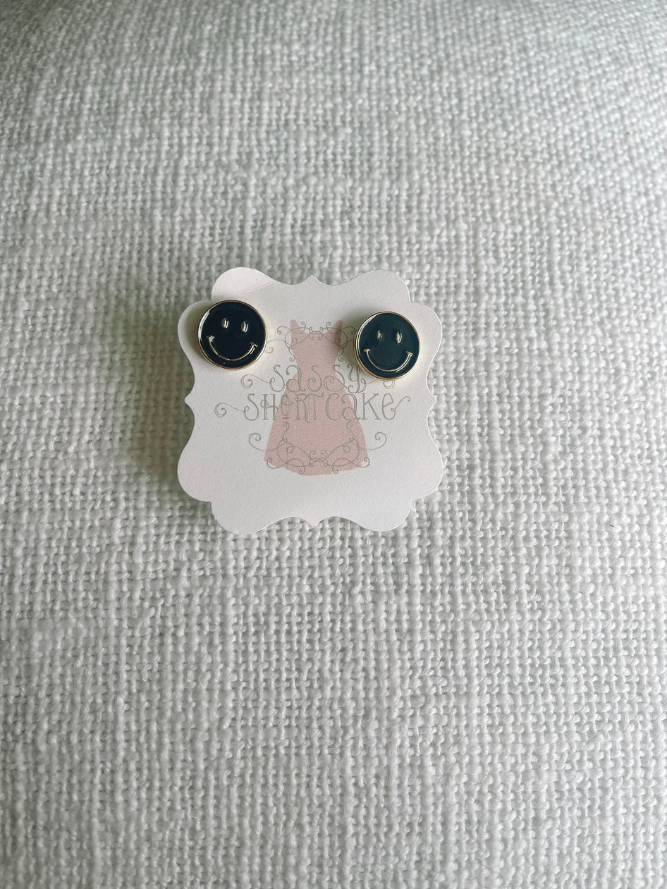 Black smiley face stud earrings displayed on a white textured background.
