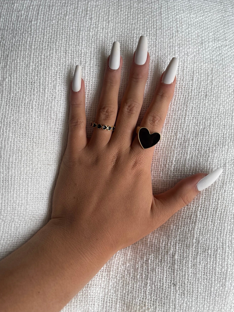 Hand model showcasing black heart rings on a white textured background.

