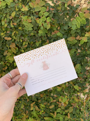Gift certificate with gold confetti design, held against a leafy green backdrop.
