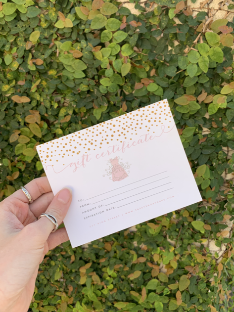 Gift certificate with gold confetti design, held against a leafy green backdrop.
