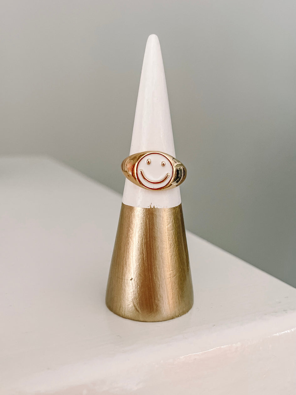 Gold smiley face ring on a white and gold display cone.

