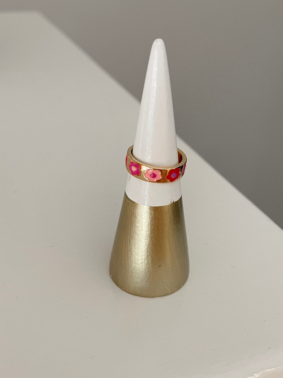 Gold band ring adorned with pink and red flowers, displayed on a two-tone ring cone.
