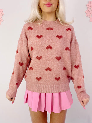 Dusty rose knit sweater adorned with embroidered hearts, modeled with a pink pleated mini skirt.
