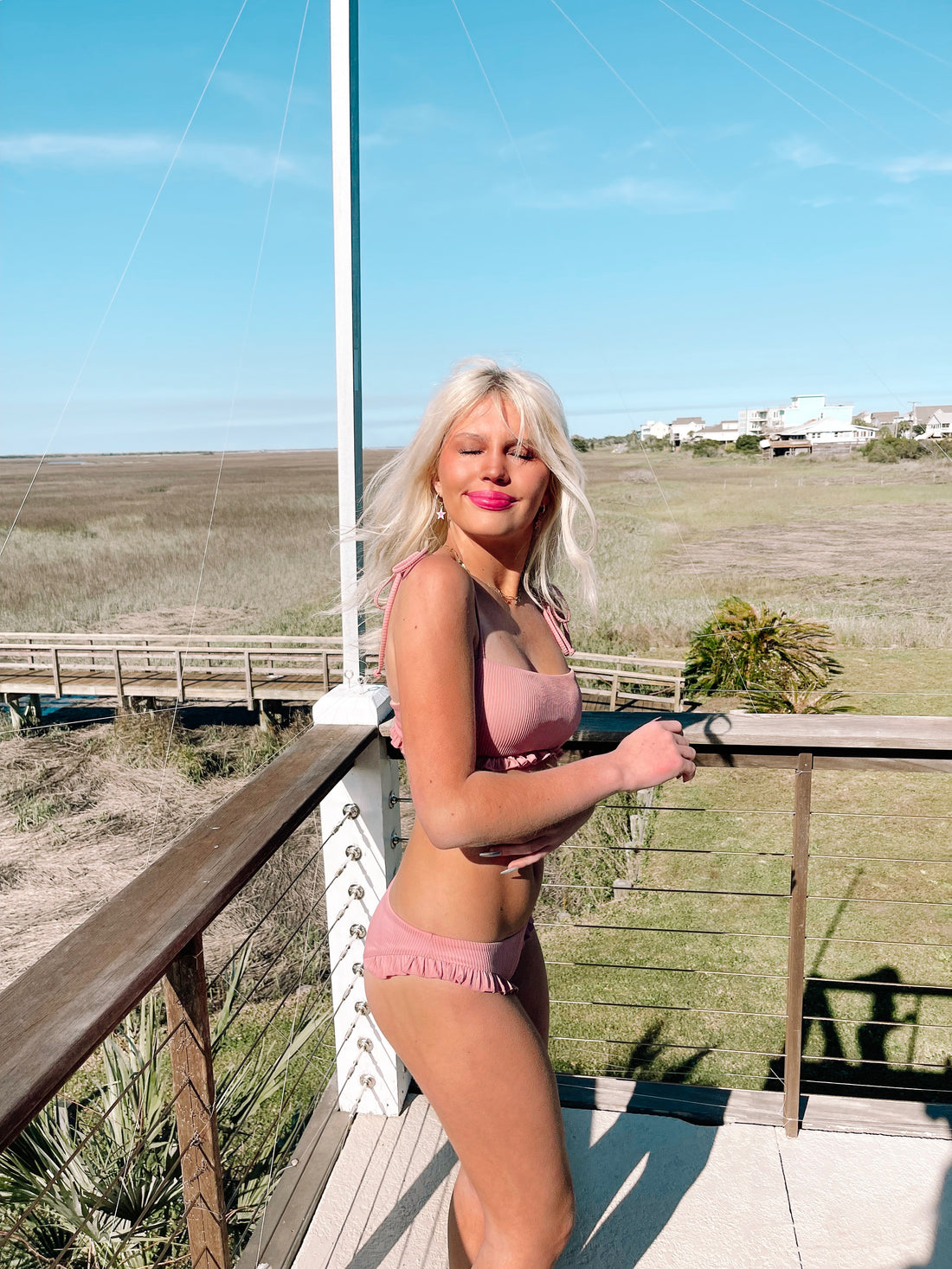 Dusty rose ruffled bikini on a sunny deck overlooking a marshy landscape.
