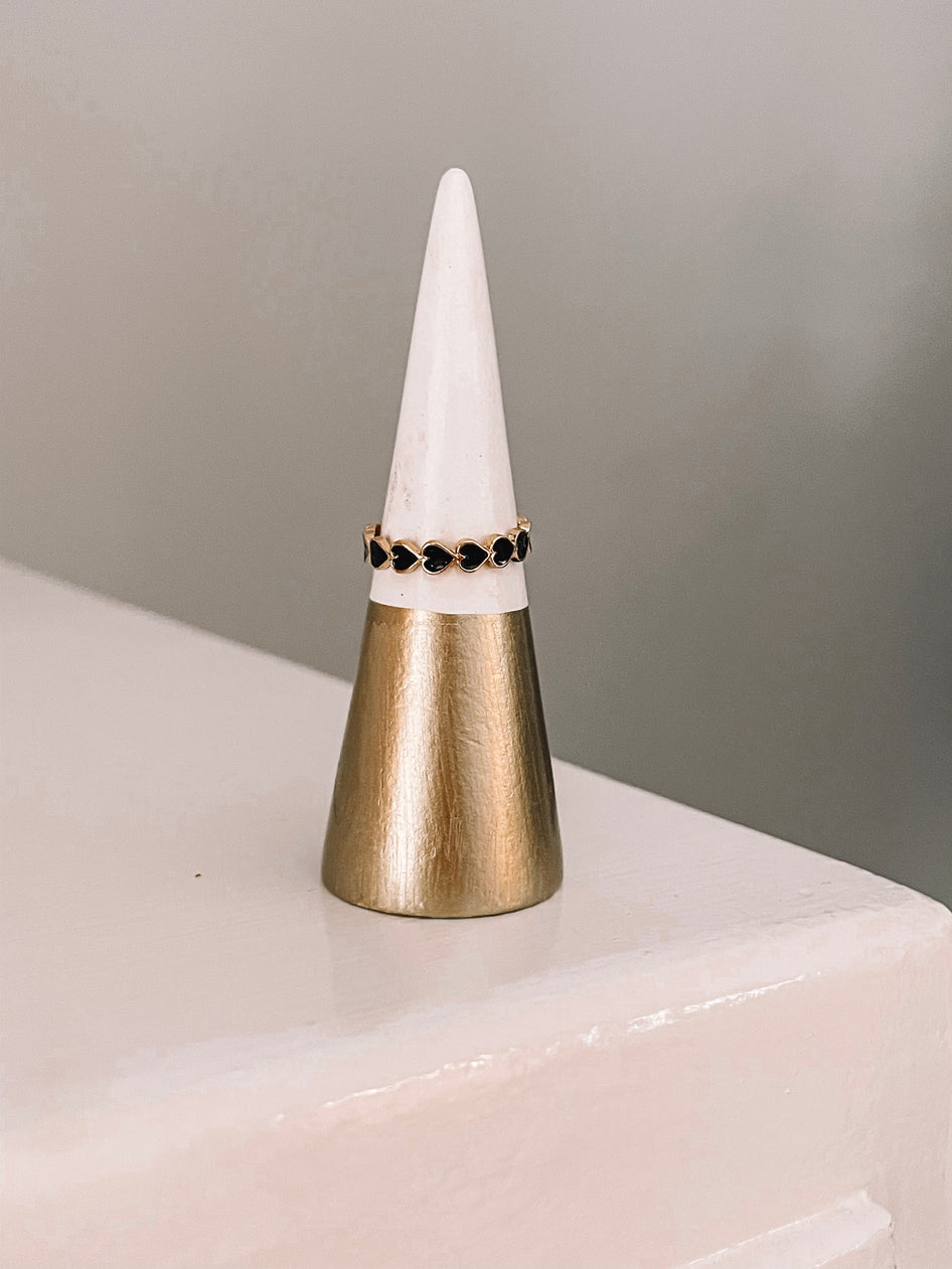 Gold ring featuring a row of black hearts, displayed on a modern ring cone.
