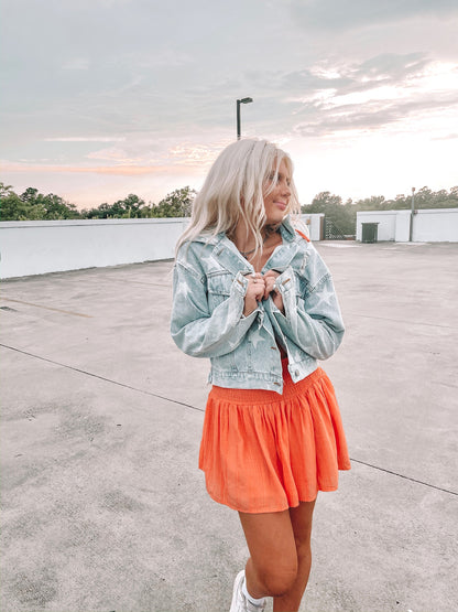 Light wash denim jacket with white star accents, worn outdoors at sunset.
