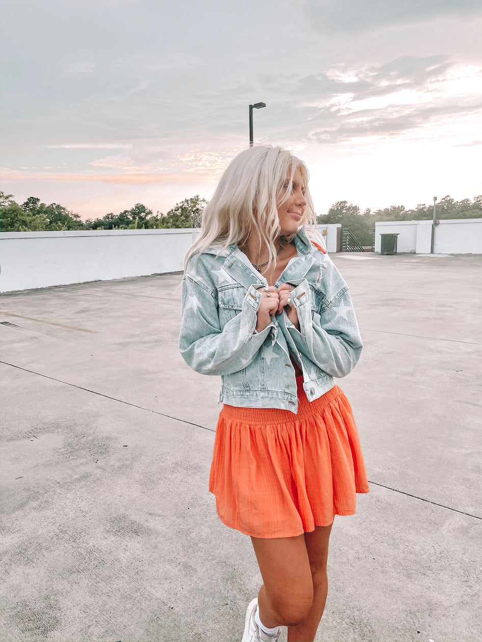 Light wash denim jacket with white star accents, worn outdoors at sunset.
