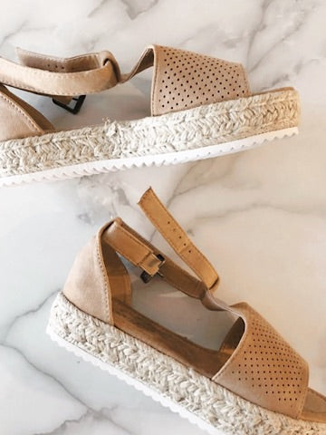 Beige perforated suede espadrille sandals with ankle strap, on marble background.
