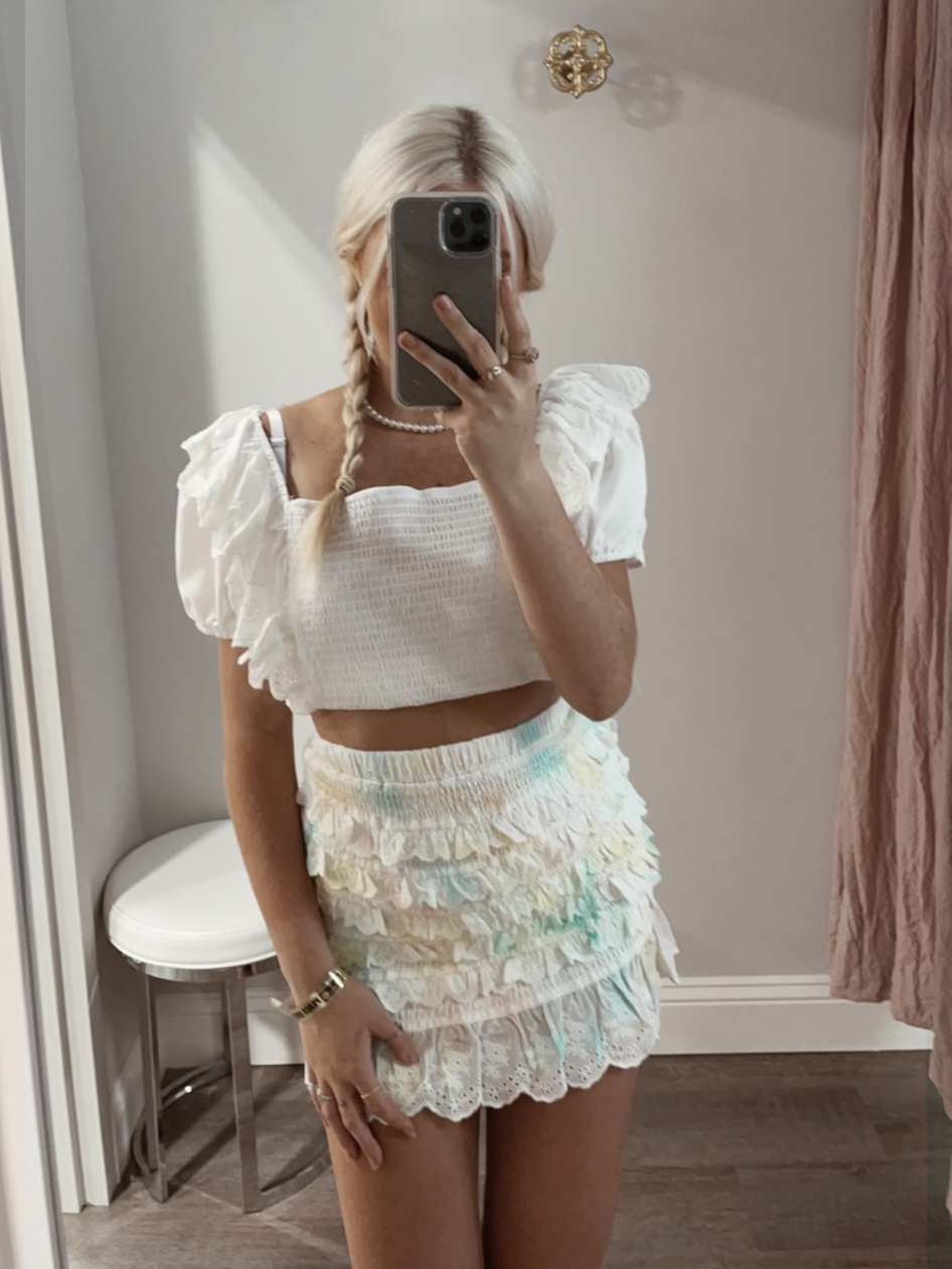 Layered pastel tie-dye mini skirt with eyelet trim, styled with a white crop top.
