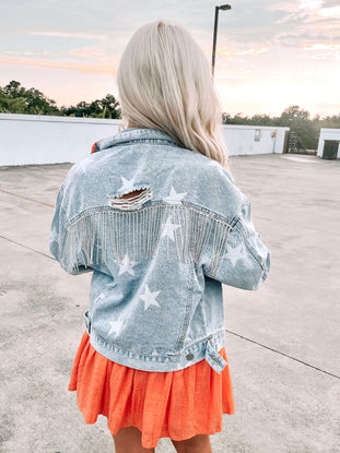Light wash denim jacket with distressed detail, embellished with rhinestones,  worn outdoors.
