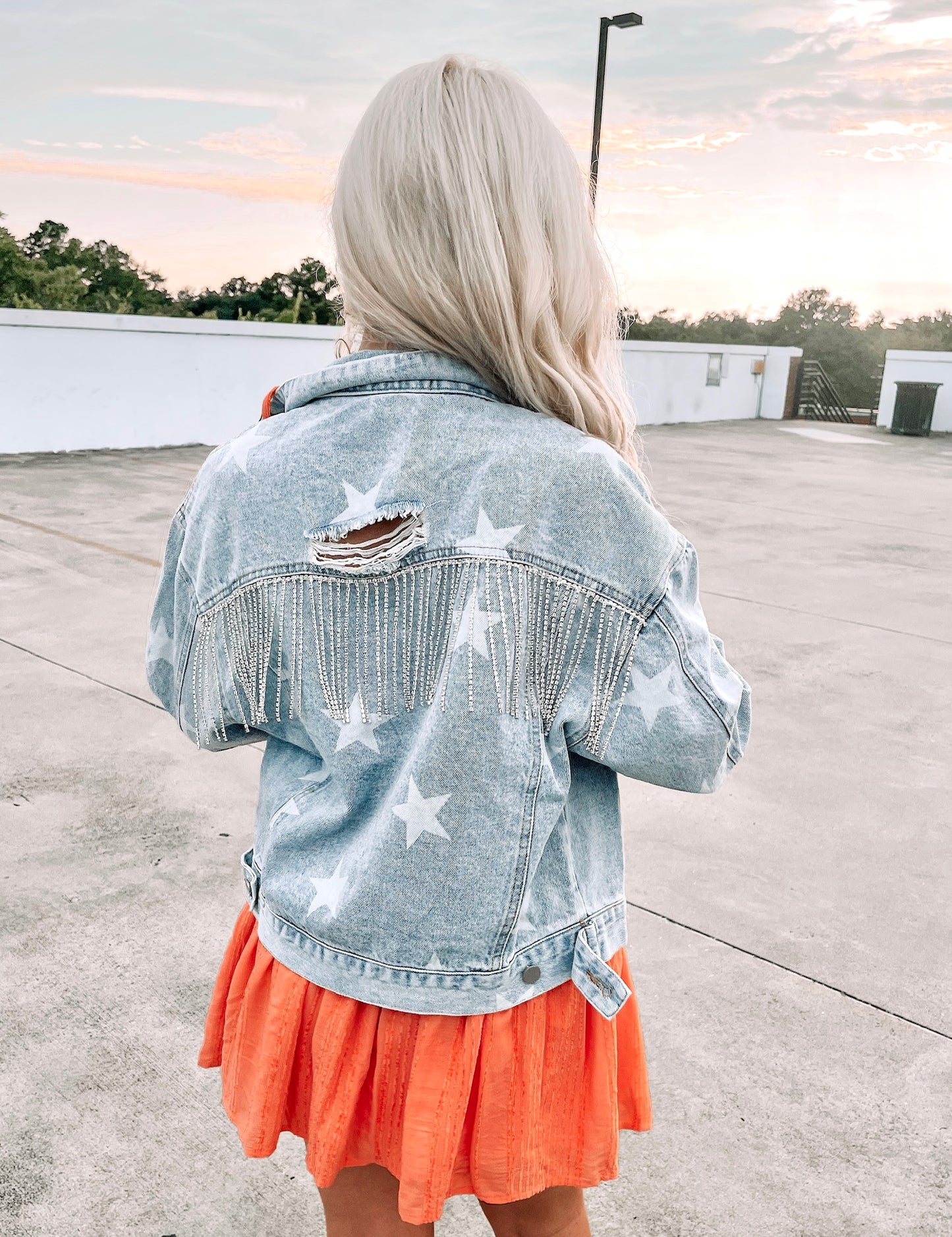 Light wash denim jacket with distressed detail, embellished with rhinestones,  worn outdoors.
