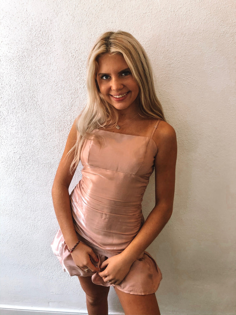 Blush pink mini dress with a ruffled hem, worn by a blonde woman against a white wall.
