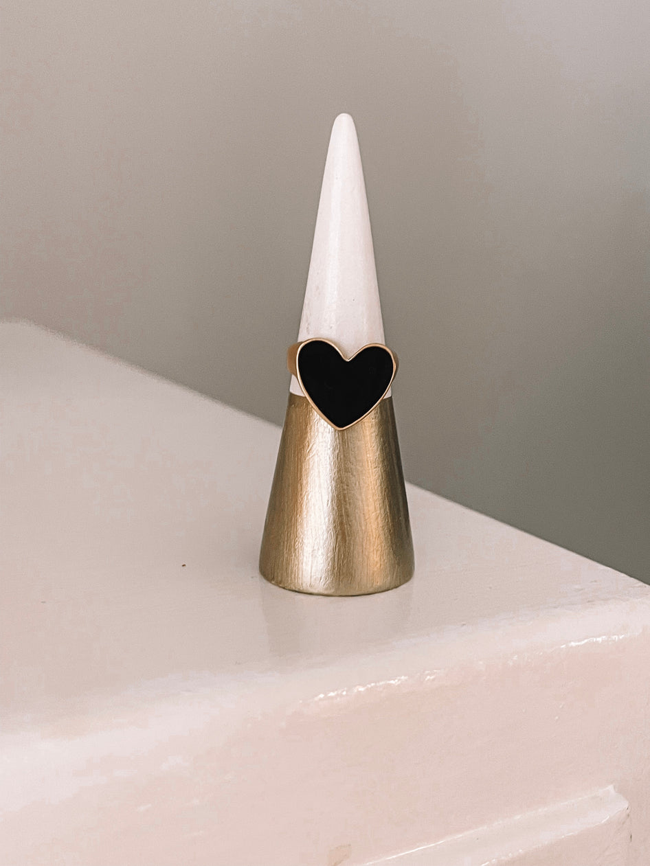 Gold heart ring with black inlay displayed on a cone-shaped stand.
