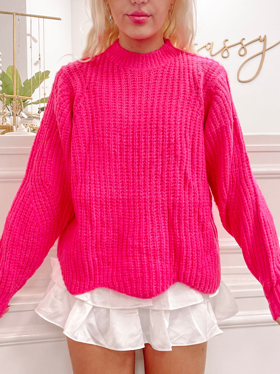 Hot pink waffle-knit sweater styled with a white ruffled skirt.
