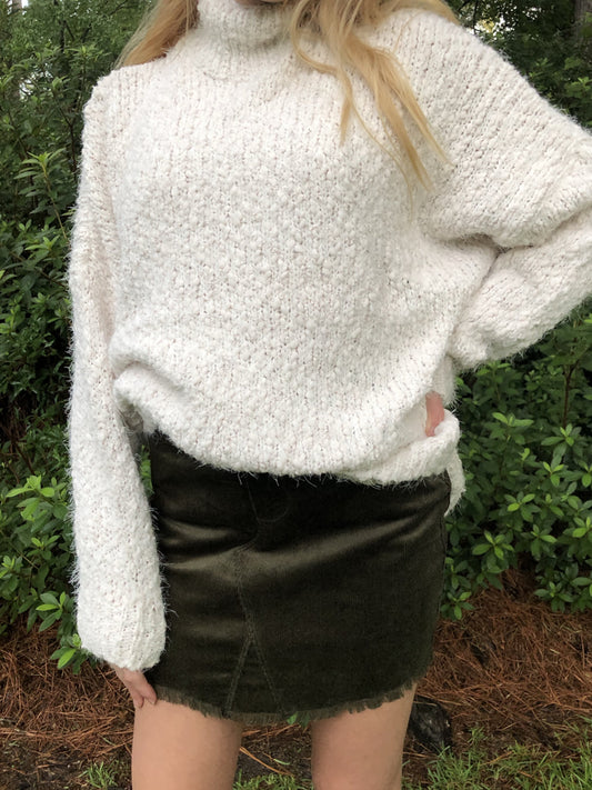 Olive green corduroy mini skirt with frayed hem, modeled with cream fuzzy sweater.
