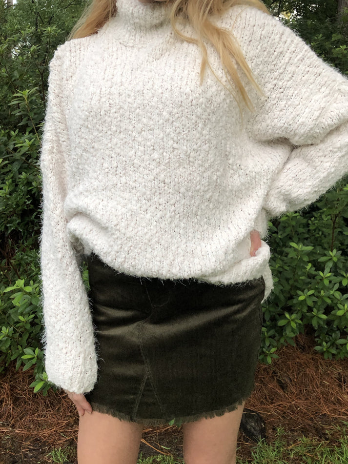 Olive green corduroy mini skirt with frayed hem, modeled with cream fuzzy sweater.
