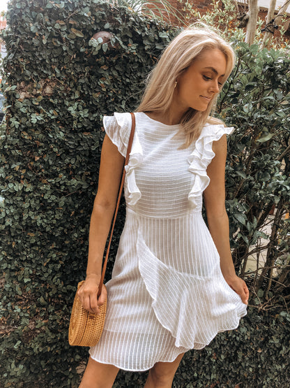 White eyelet mini dress with ruffled sleeves, styled outdoors against lush greenery.
