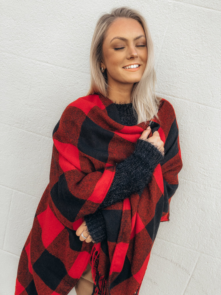 Red and black buffalo plaid poncho draped over a model against a white wall.
