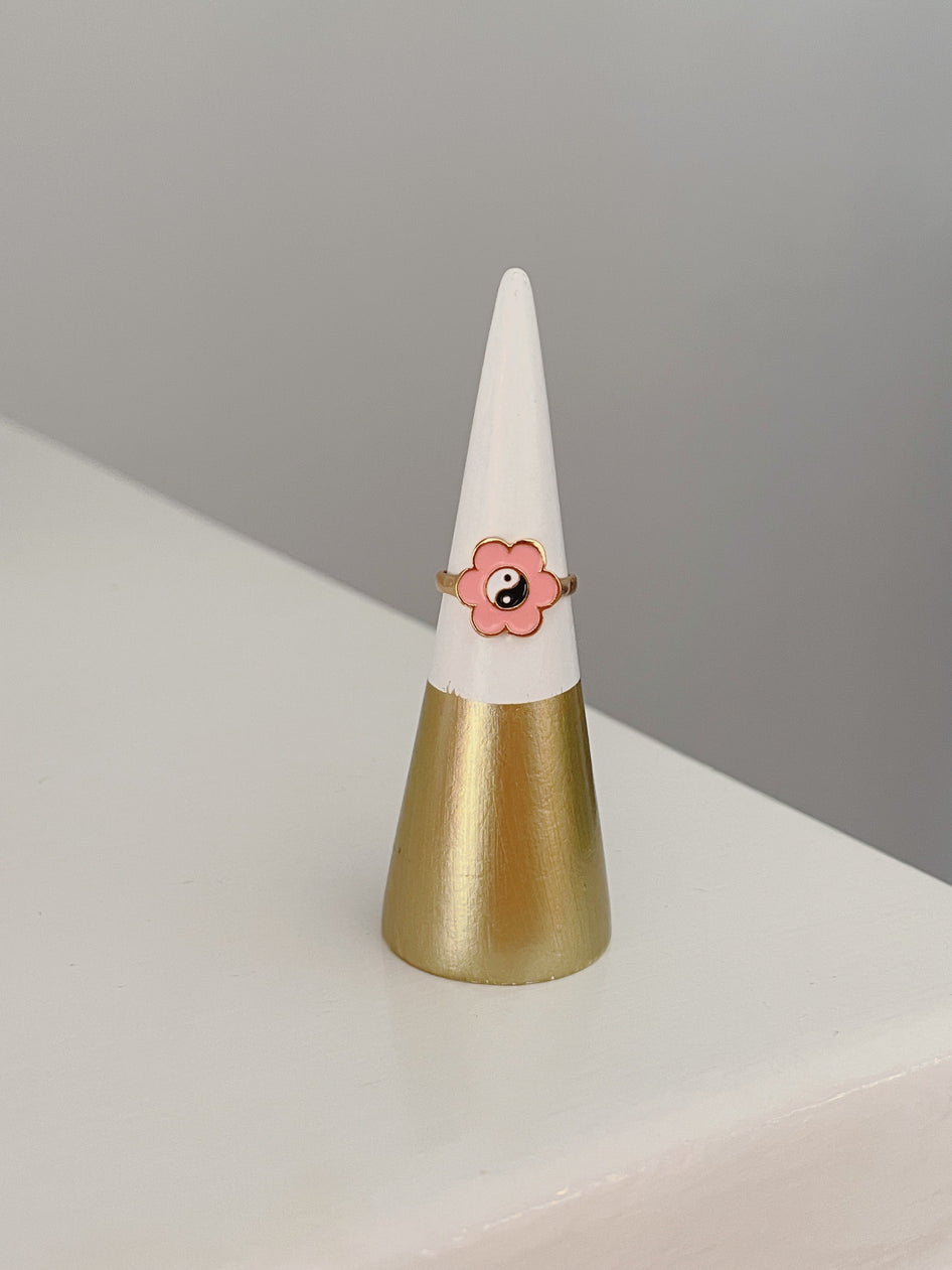 Pink flower ring with yin-yang detail, displayed on a gold and white cone.
