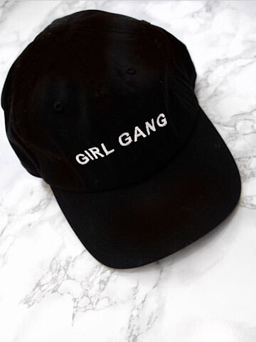 Black baseball cap with "Girl Gang" embroidered in white.

