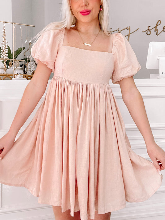 Pink linen mini dress with puff sleeves and a square neckline, shown on a model.