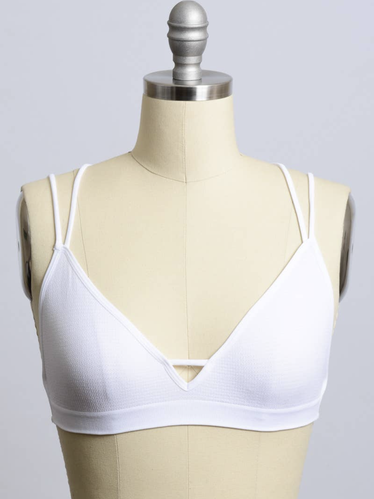 White bralette with double straps on a dress form, against a neutral background.
