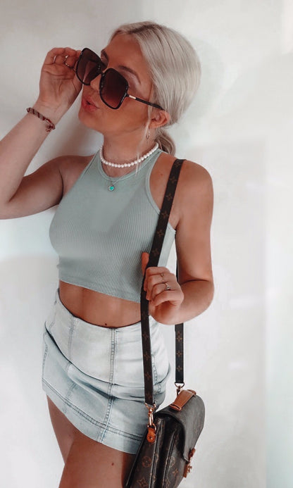 Woman in light blue ribbed tank top and denim skirt, accessorized with sunglasses and pearl necklace.
